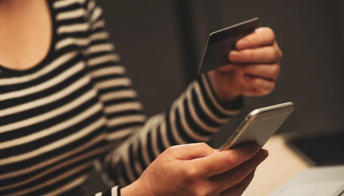 Pessoa com um celular e um cartão na mão, representando uma compra online.