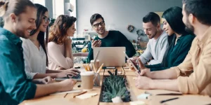 equipe de marketing fazendo reunião com seu gestor de tráfego orgânico, são um total de 6 funcionários e o gestor sentado na cadeira principal, dentro da sala de reuniões.