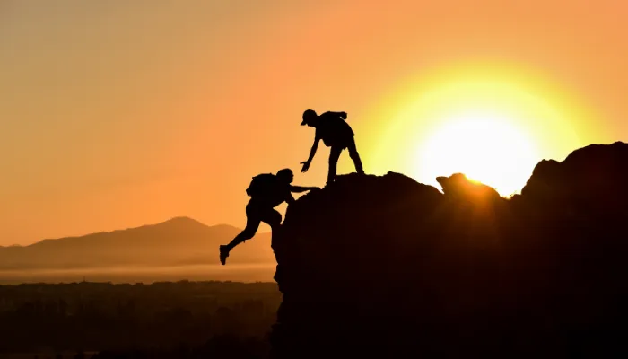 imagem de dois homens acima da montanha, no topo, onde o de cima pega a mão do de baixo, ajudando-o, mostrando construindo a confiança no mundo dos seguros empresariais.