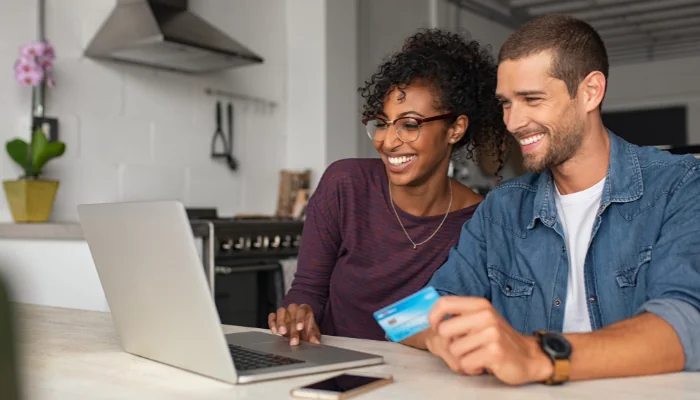 Como Configurar Pagamento no Mercado Pago representado por duas pessoas em frente ao computador com um cartão em mãos.