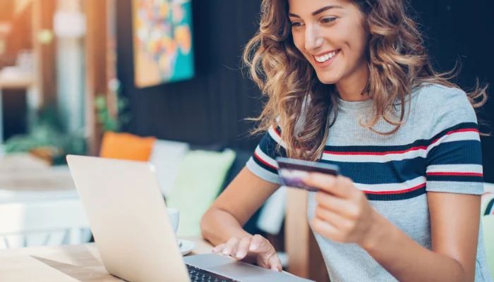 Quais são os gateways de pagamento representado por uma mulher sorrindo com um cartão na mão na frente do computador.